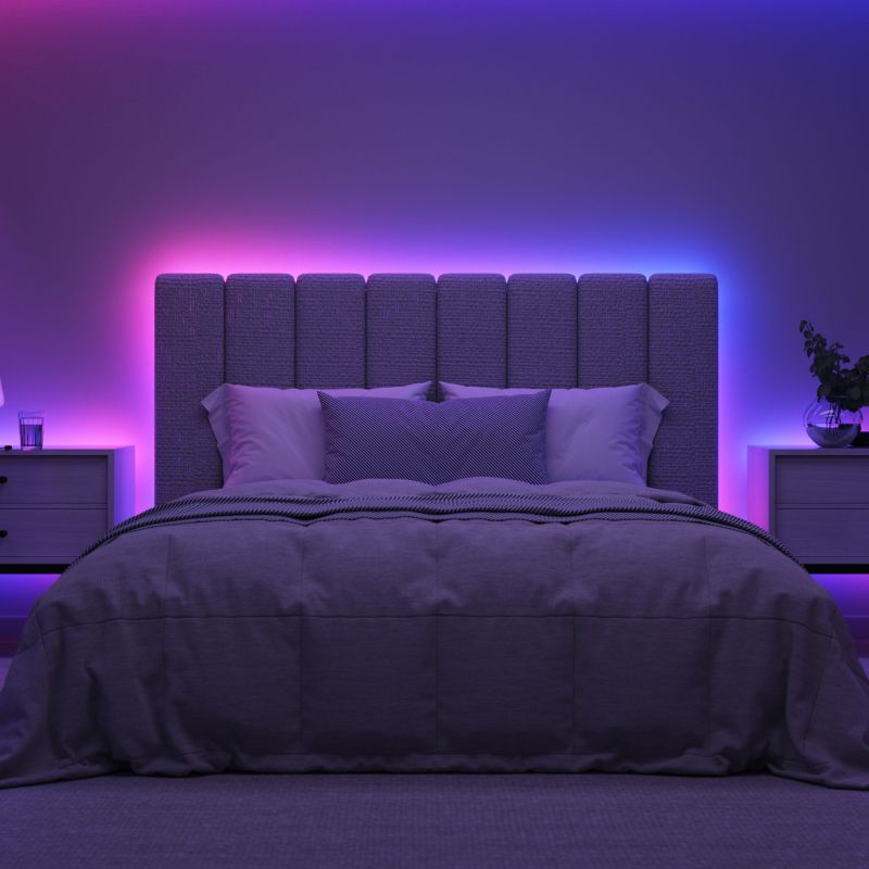 Outdoor string lights in purple and blue hues hanging from a pole on a wooden patio with a scenic mountain view. Coffee table with a tray of two drinks and a plate. A corner bench chair with surrounding greenery and plants.